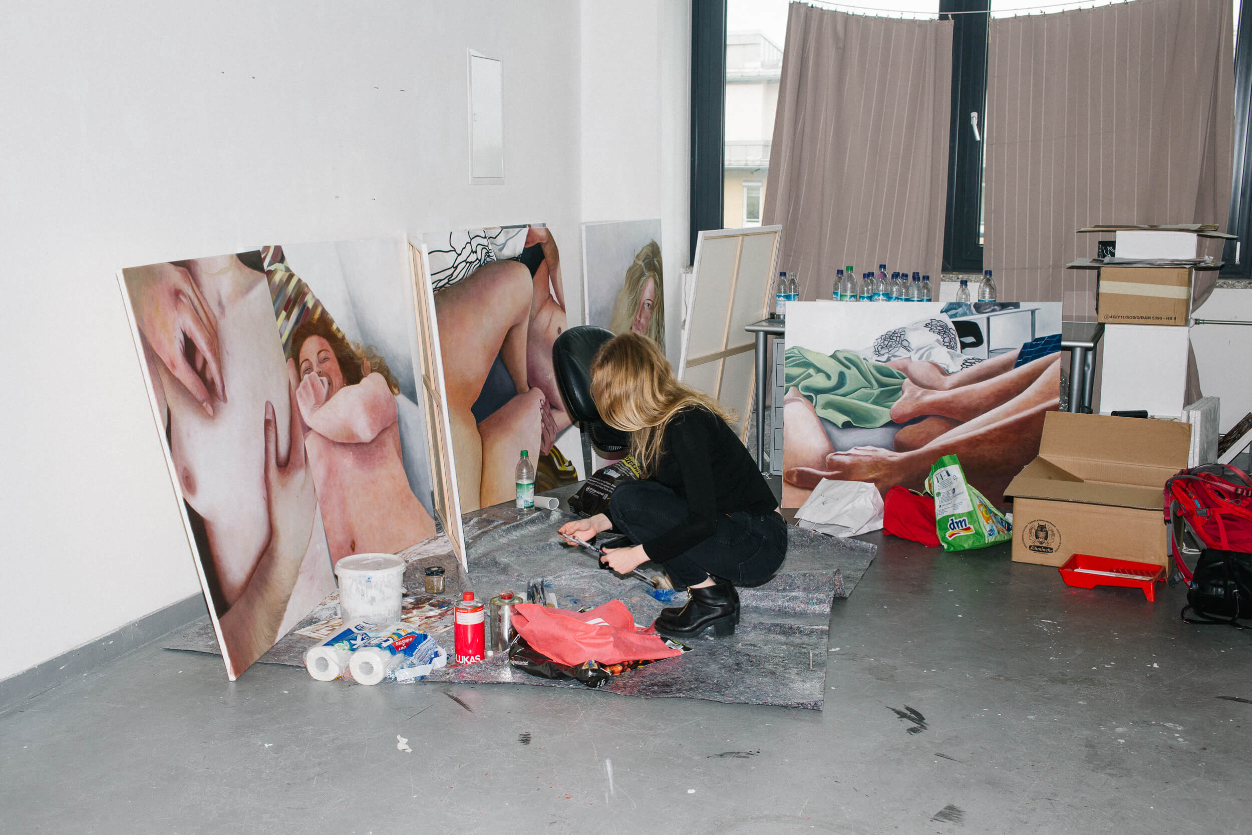 Die künstlerin kniet vor ihren Gemälden, die auf dem Boden an die Wand gelehnt sind. Sie mischt gerade Farben an.